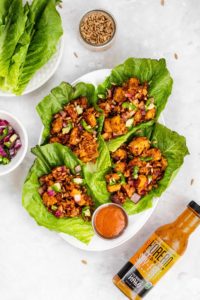 Lettuce wraps filled with seasoned meat, onions, and herbs, served with dipping sauce and a bottle of hot sauce.