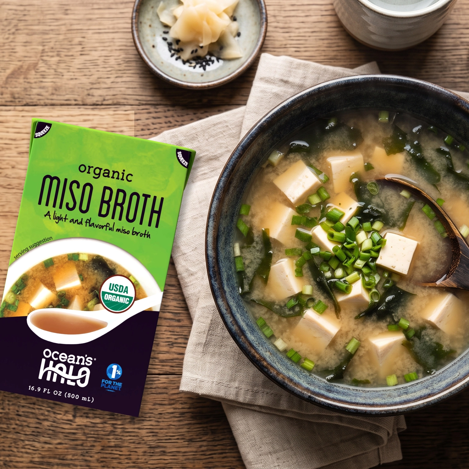 A bowl of miso soup with tofu and seaweed next to Ocean's Halo Miso Broth carton on a wooden table.
