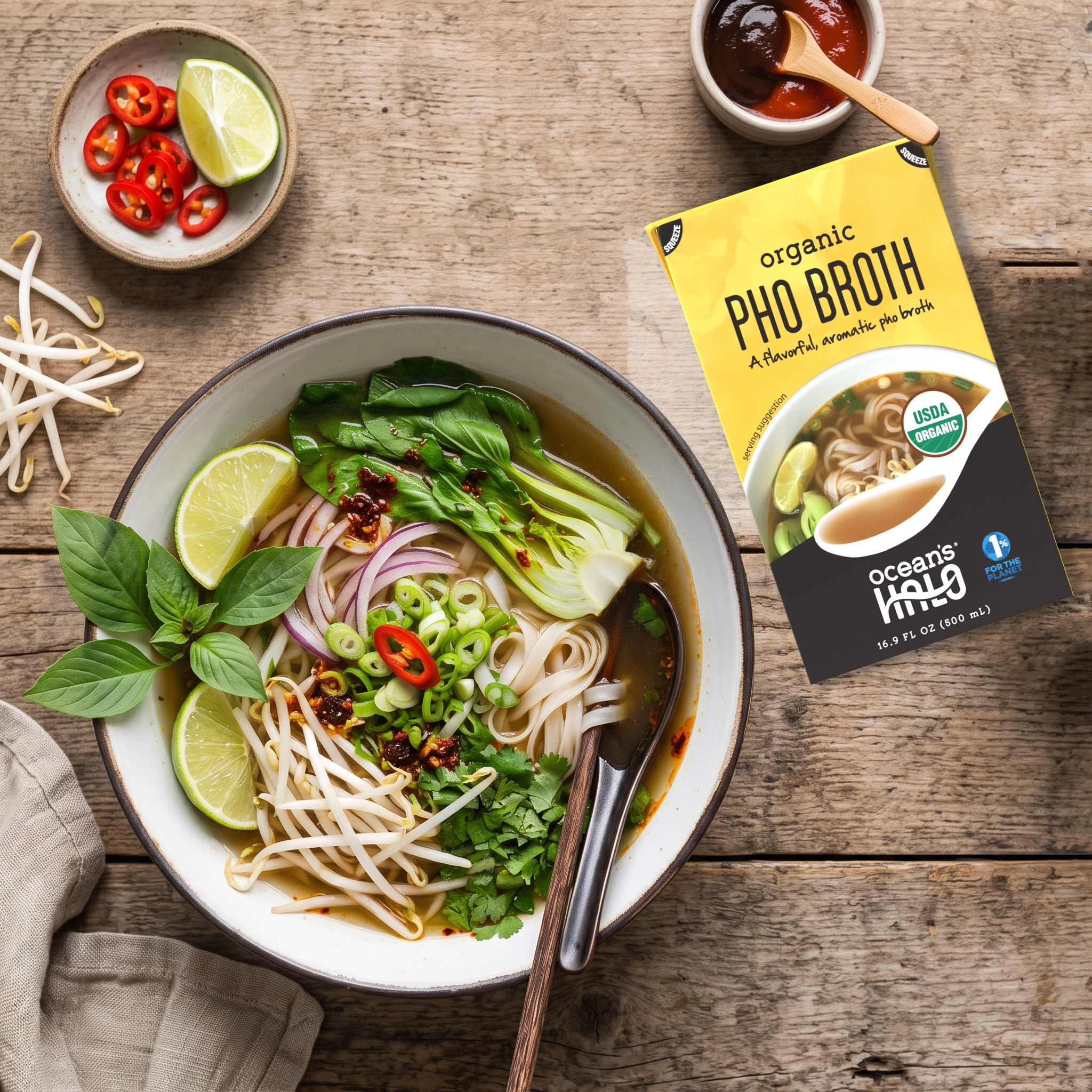 A bowl of homemade pho next to Ocean's Halo Pho Broth carton on a rustic wooden table.