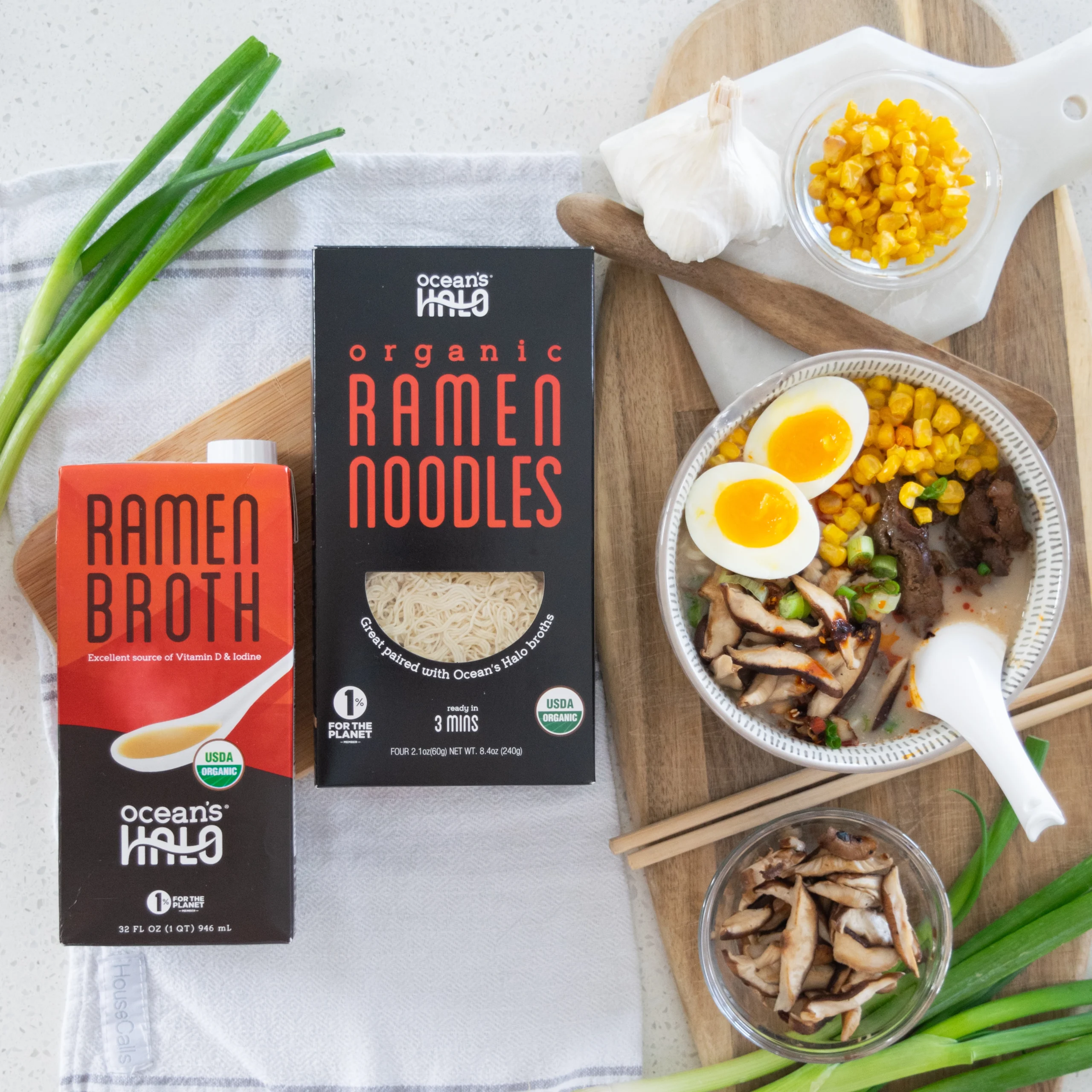 Bowl of ramen with soft-boiled egg and toppings next to Ocean's Halo Ramen Broth and Organic Ramen Noodles packaging.