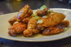A plate of chicken wings garnished with sesame seeds and chopped green onions, showcasing a delicious and appetizing dish.