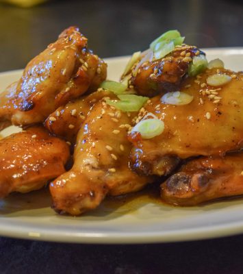 A plate of chicken wings garnished with sesame seeds and chopped green onions, showcasing a delicious and appetizing dish.