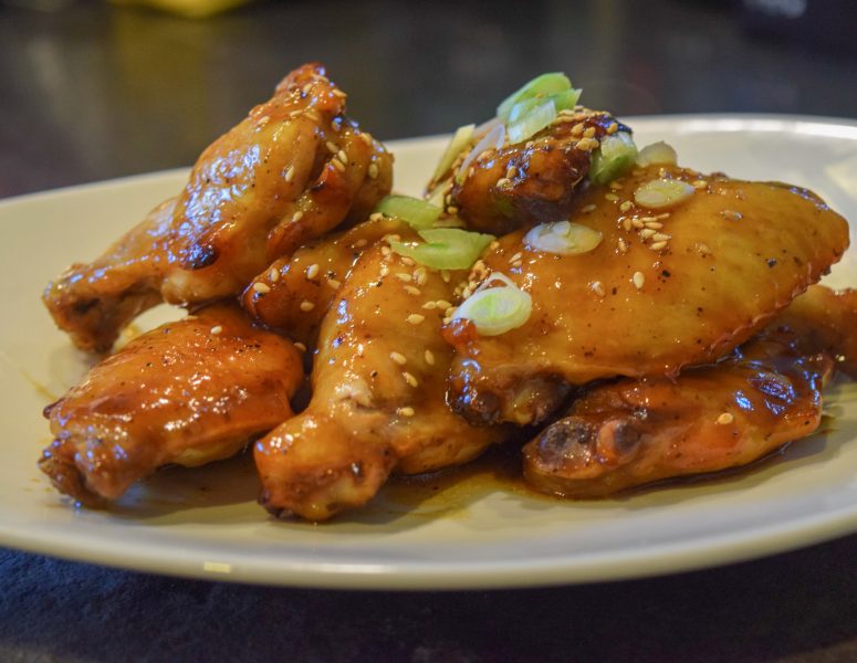 A plate of chicken wings garnished with sesame seeds and chopped green onions, showcasing a delicious and appetizing dish.