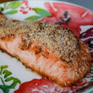 A plate featuring a piece of salmon topped with a light sprinkle of cheese, elegantly presented for a meal.
