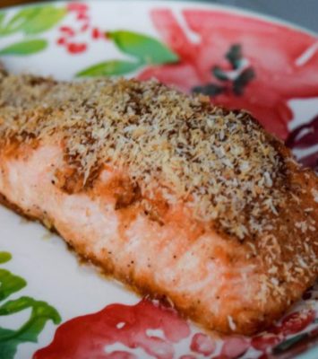 A plate featuring a piece of salmon topped with a light sprinkle of cheese, elegantly presented for a meal.