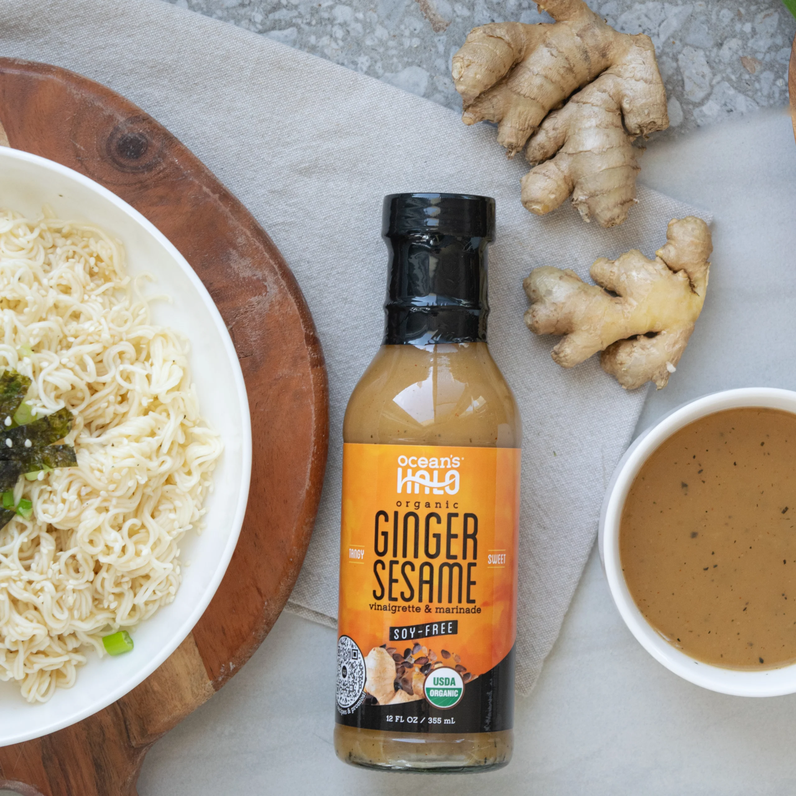 Ramen noodles in a bowl next to fresh ginger root and a bottle of Ocean's Halo Ginger Sesame Dressing.