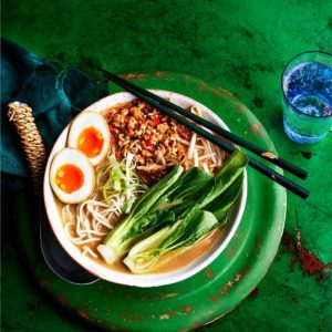 A bowl of ramen topped with a soft-boiled egg, accompanied by a pair of chopsticks resting beside it.