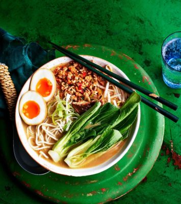 A bowl of ramen topped with a soft-boiled egg, accompanied by a pair of chopsticks resting beside it.