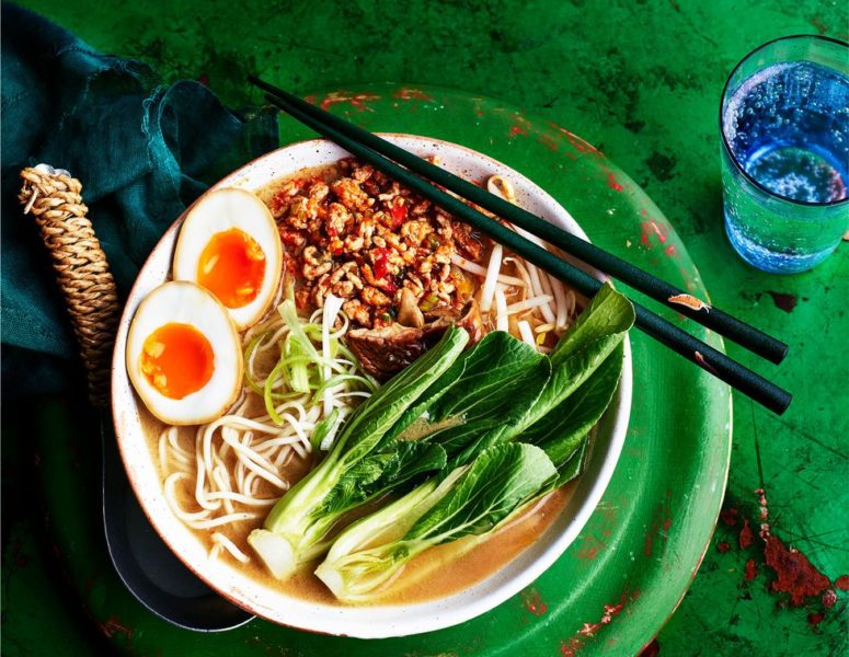 A bowl of ramen topped with a soft-boiled egg, accompanied by a pair of chopsticks resting beside it.