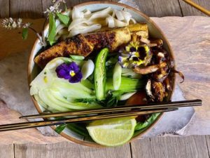 A bowl filled with noodles and colorful vegetables, accompanied by a pair of chopsticks resting on the side.
