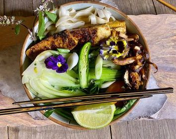 A bowl filled with noodles and colorful vegetables, accompanied by a pair of chopsticks resting on the side.