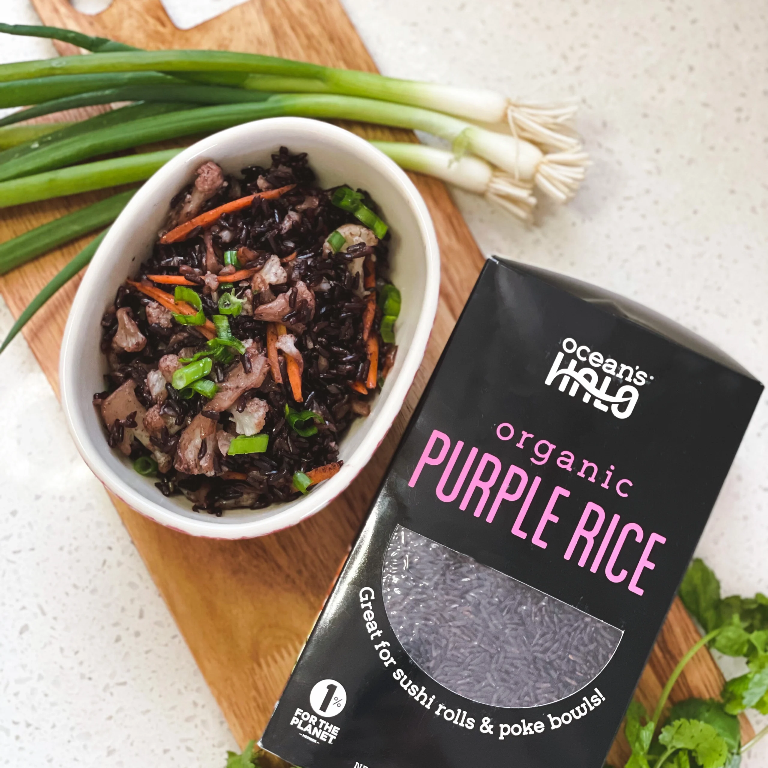 Bowl of cooked purple rice with scallions served alongside a box of Ocean's Halo Organic Purple Rice.