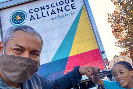 A man taking a selfie with a kid in front of a trunk with Conscious Alliance art that feeds
