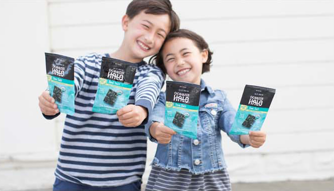 Two happy smiling kids holding Ocean’s Halo Sea Salt Seaweed Snacks.