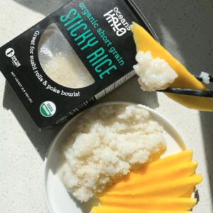 A plate of rice topped with fresh mango slices beside a box of organic rice.