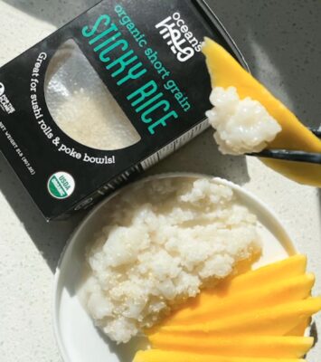 A plate of rice topped with fresh mango slices beside a box of organic rice.