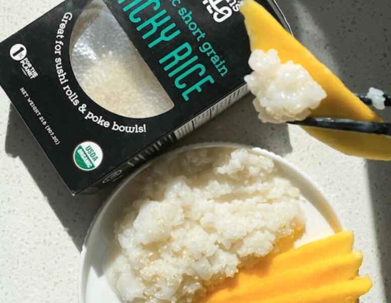 A plate of rice topped with fresh mango slices beside a box of organic rice.