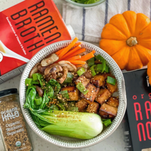 A bowl filled with fresh vegetables sits beside an open book on a wooden table.