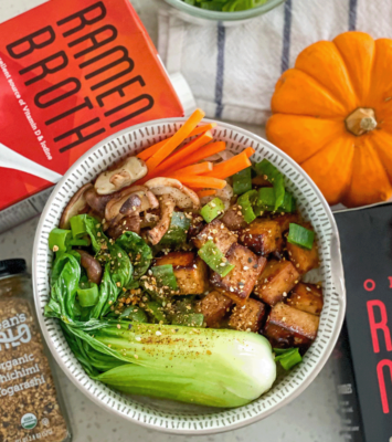 A bowl filled with fresh vegetables sits beside an open book on a wooden table.