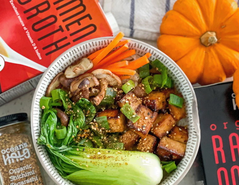 A bowl filled with fresh vegetables sits beside an open book on a wooden table.