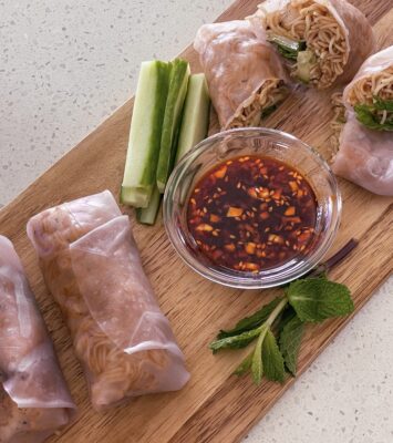 A wooden cutting board featuring a bowl of sauce alongside freshly baked rolls.
