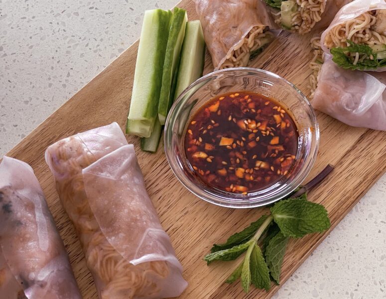 A wooden cutting board featuring a bowl of sauce alongside freshly baked rolls.