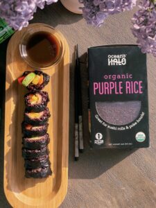 A box of organic purple rice beside a plate of sushi, showcasing a vibrant and healthy meal option.