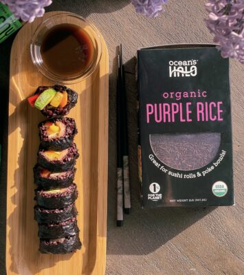 A box of organic purple rice beside a plate of sushi, showcasing a vibrant and healthy meal option.