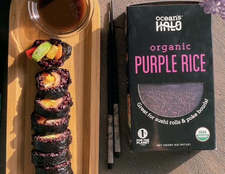 A box of organic purple rice beside a plate of sushi, showcasing a vibrant and healthy meal option.