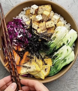 A bowl filled with rice, colorful vegetables, and tofu, showcasing a healthy and vibrant meal.