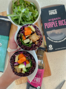 Two purple rice wraps filled with fresh vegetables and herbs, elegantly arranged on a plate.
