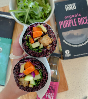 Two purple rice wraps filled with fresh vegetables and herbs, elegantly arranged on a plate.