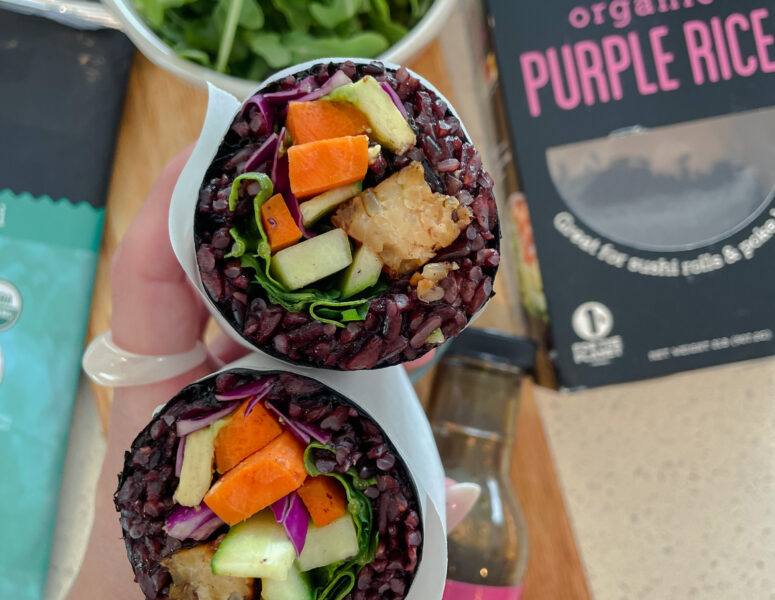 Two purple rice wraps filled with fresh vegetables and herbs, elegantly arranged on a plate.