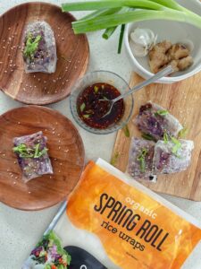 A plate of crispy spicy chicken spring rolls garnished with fresh herbs and served with a dipping sauce.