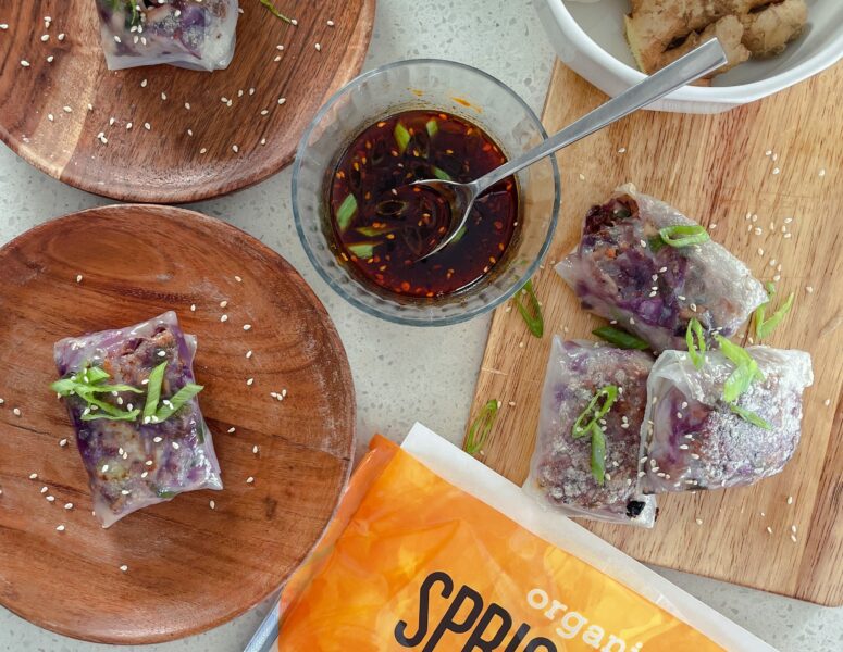 A plate of crispy spicy chicken spring rolls garnished with fresh herbs and served with a dipping sauce.