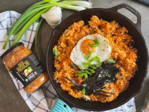 A bowl of Korean fried rice topped with a perfectly cooked egg, garnished with green onions and sesame seeds.