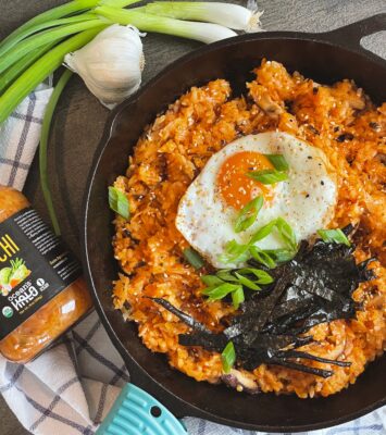 A bowl of Korean fried rice topped with a perfectly cooked egg, garnished with green onions and sesame seeds.