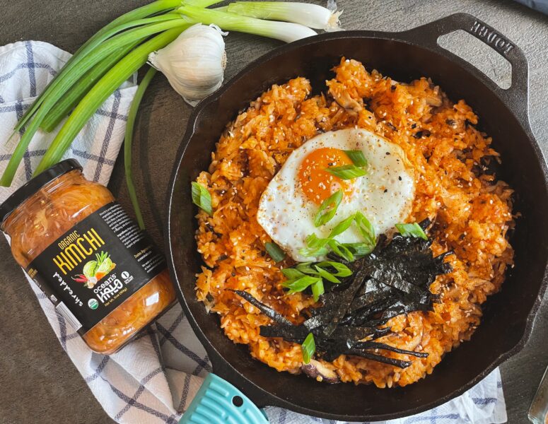 A bowl of Korean fried rice topped with a perfectly cooked egg, garnished with green onions and sesame seeds.
