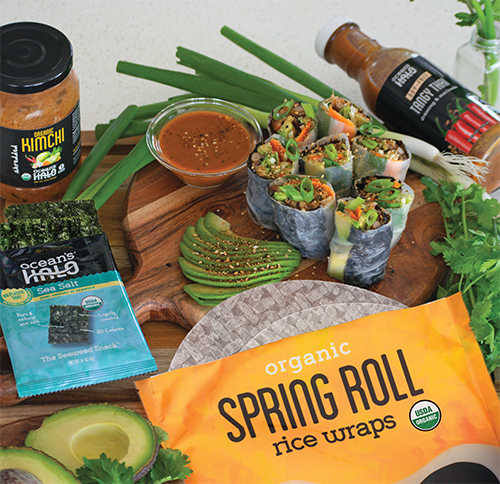 Summer rolls sliced on a cutting board next to Ocean’s Halo Spring roll wraps, dressing, Sea salt seaweed, & Kimchi.