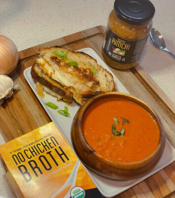 A plate with Tomato Soup and Kimchi Grilled cheese on it with Ocean’s Halo No Chicken Broth and Kimchi next to it.