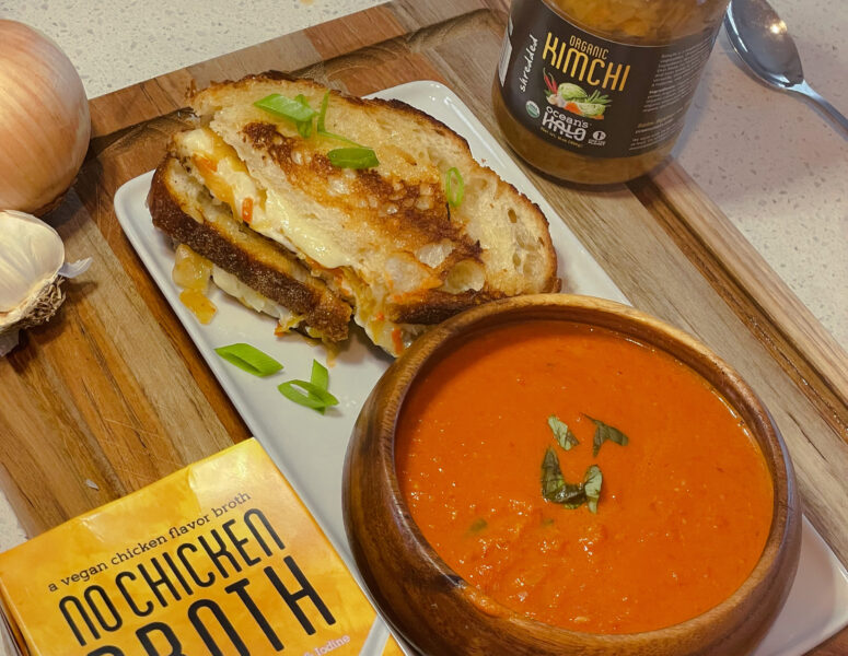 A plate with Tomato Soup and Kimchi Grilled cheese on it with Ocean’s Halo No Chicken Broth and Kimchi next to it.