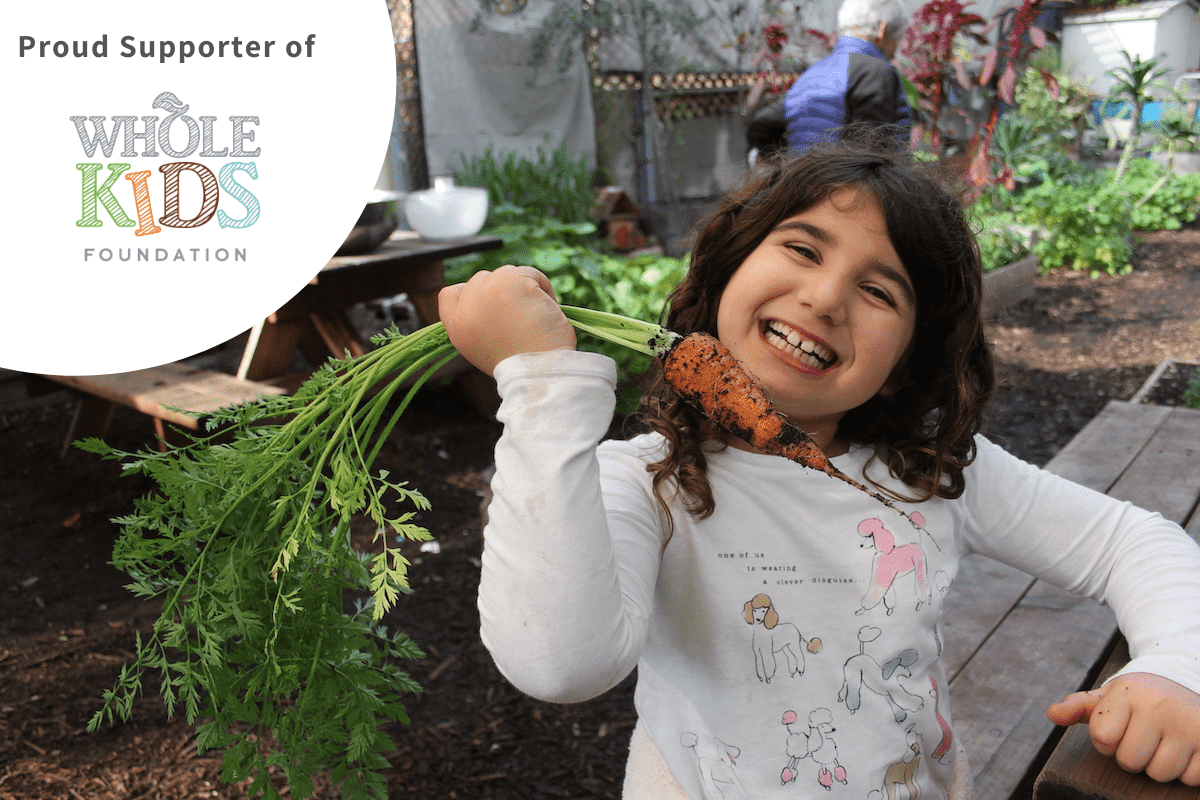 Proud supporter of Whole Kids Foundation. A smiling girl holding a freshly picked carrot in a farm.