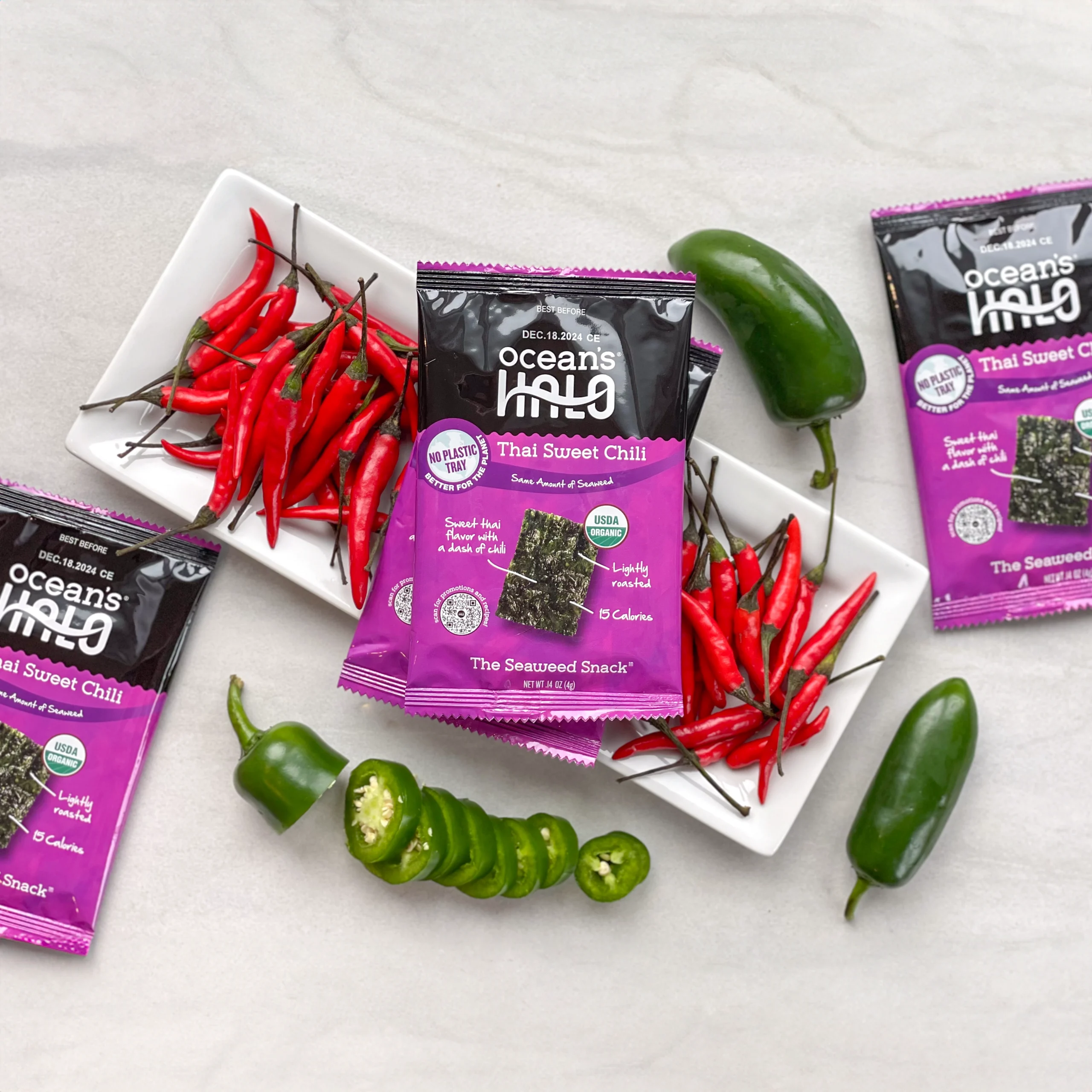 Ocean's Halo Thai Sweet Chili seaweed snack packages arranged with fresh red chilis and sliced jalapeños.