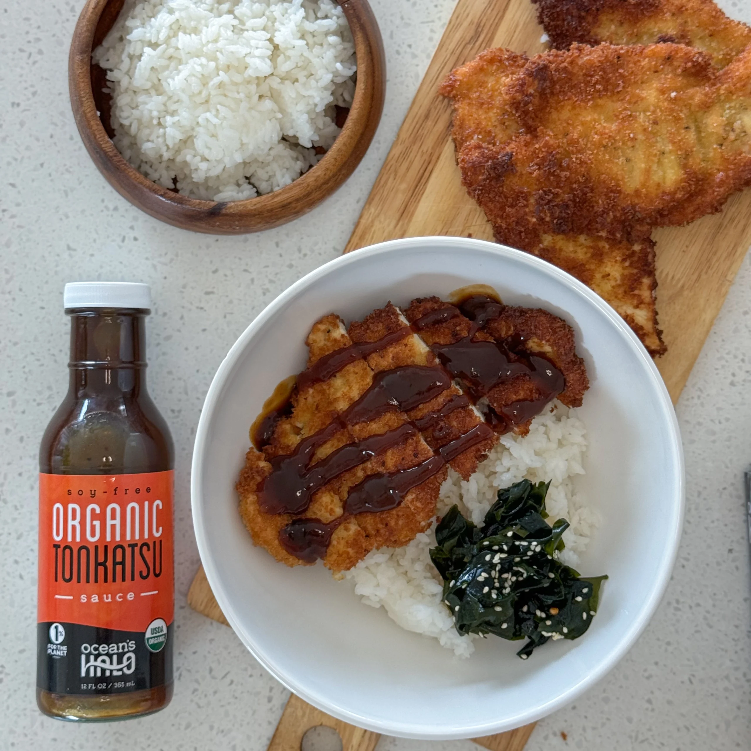 Chicken katsu drizzled with sauce over white rice next to a bottle of Ocean's Halo Organic Tonkatsu Sauce.