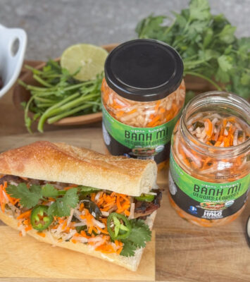 A banh mi sandwich next to jars of Ocean's Halo Banh Mi pickled vegetables.