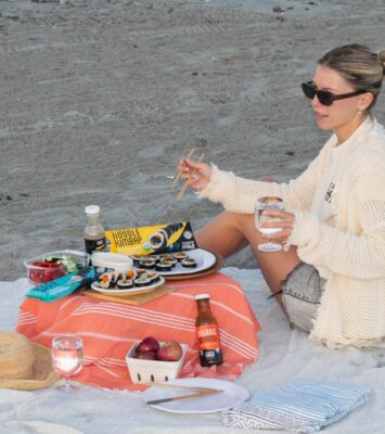 A woman on a beach blanket with a picnic of Kimbao, fruit, and Ocean's Halo seaweed snacks.