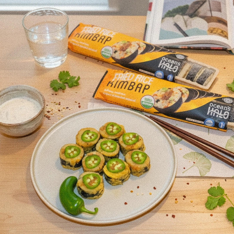 Plate of fried rice roll slices topped with jalapeño rounds, served next to Ocean's Halo packaging, dipping sauce, and water.