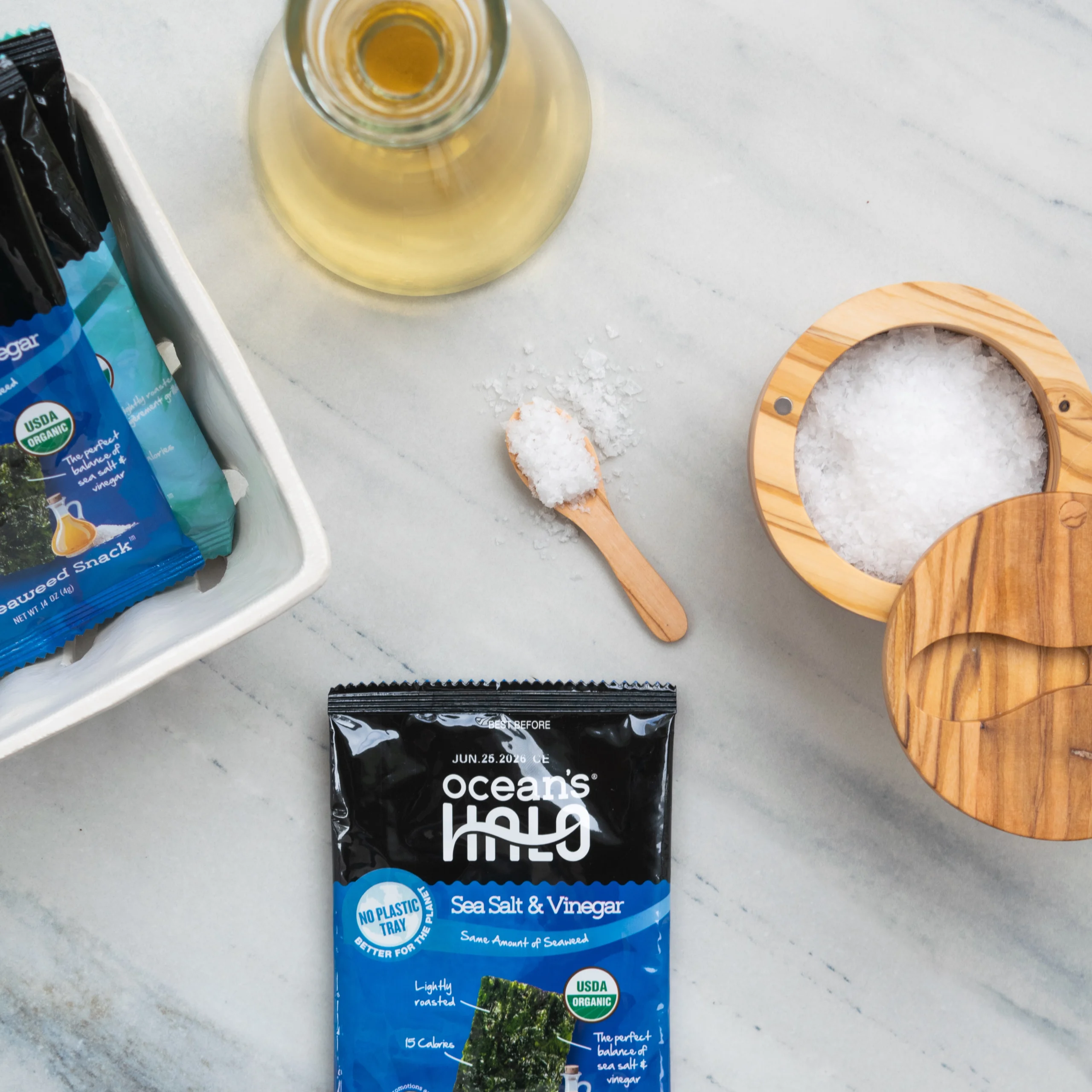 Ocean's Halo Sea Salt & Vinegar seaweed snack package next to a wooden salt cellar, salt spoon, and oil dispenser.
