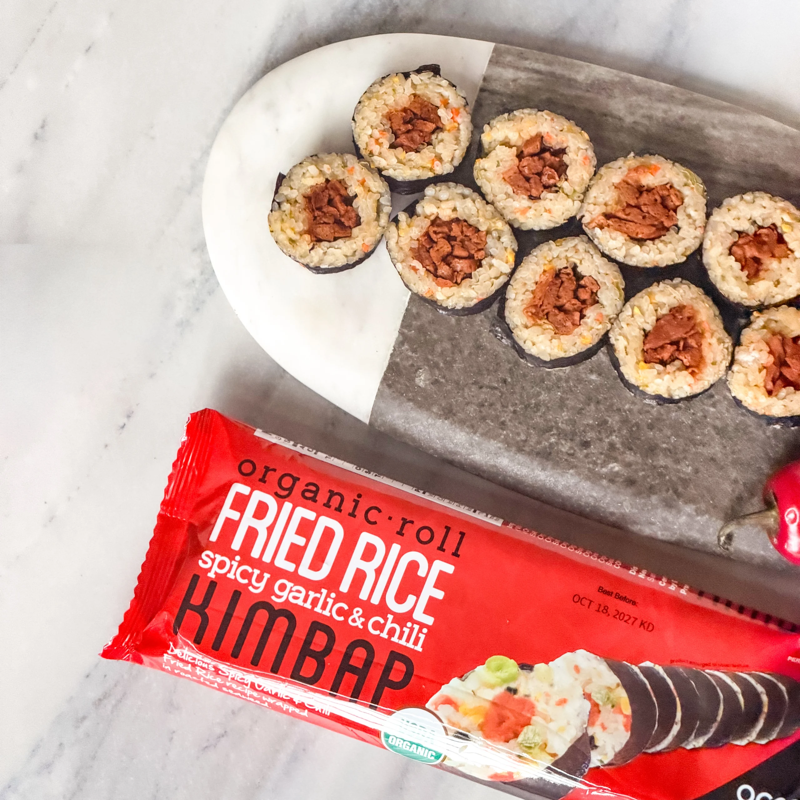 Red package of Ocean's Halo Spicy Garlic & Chili Fried Rice Roll next to sliced pieces on a two-tone stone platter.