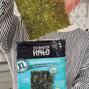 a woman pulling out an extra large seaweed snack from a package labeled as organic XL seaweed snacks. Sea Salt & avocado oil flavor.